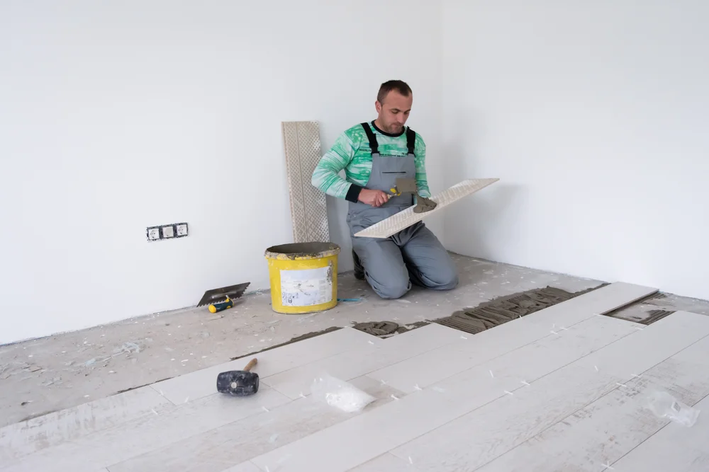 Facharbeiter, der die keramischen Holzeffektfliesen auf dem FußbodenLaminatfußboden des Arbeiter Herstellers auf der Baustelle der neuen Wohnung installiert